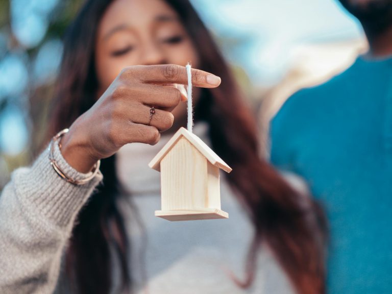 Close-up of a woman holding a wooden house symbolizing real estate or homeownership.